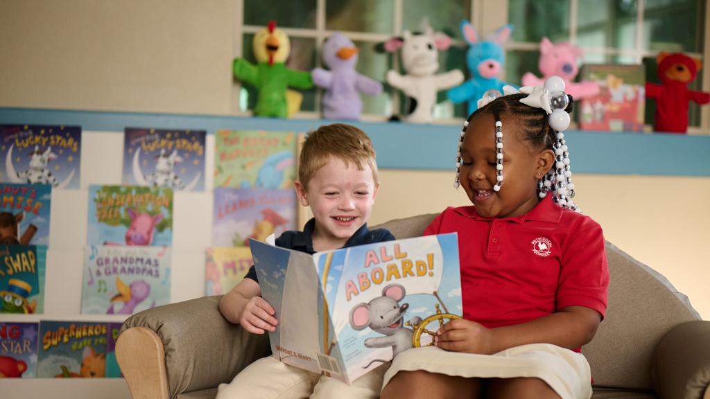 Two Primrose Schools preschool children reading All Aboard picture book together in cozy classroom library by Primrose School at Vista Ridge