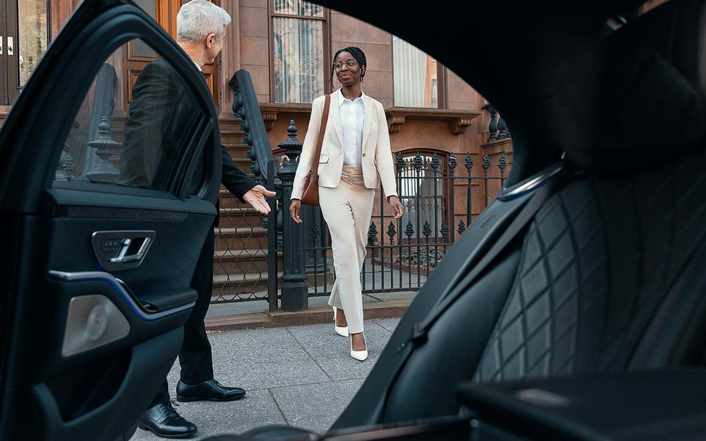 A professional chauffeur holding open the door of a luxury limousine, representing reliable airport transportation services in NYC with punctual, courteous, and comfortable service. by Automotive Luxury Limo and Car Service