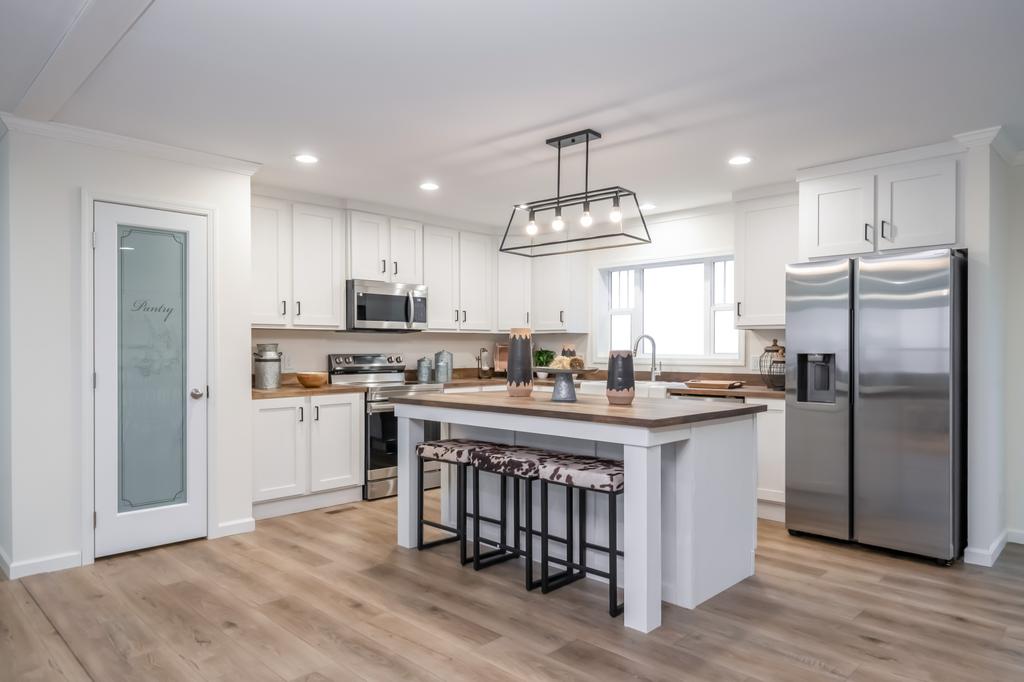 This modern manufactured home's kitchen features a central island with seating, pendant lighting, stainless steel appliances, and an attached pantry. by Clayton Homes