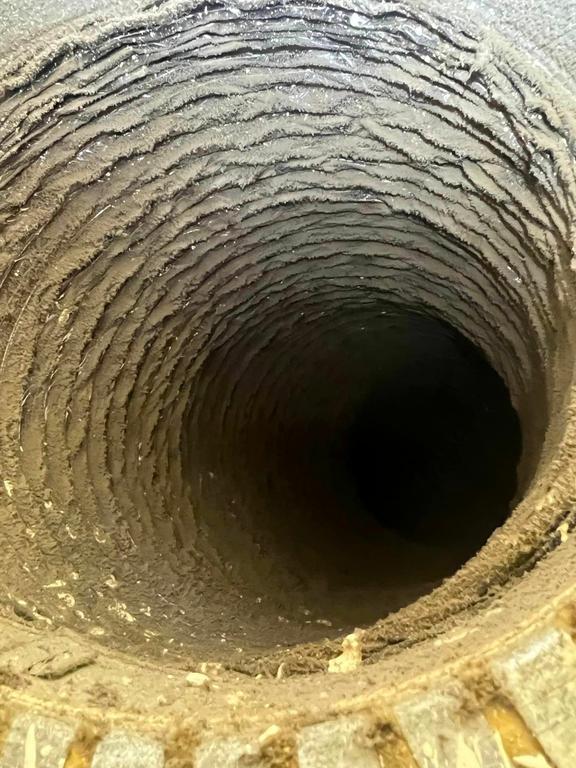 This close-up interior view of an air duct shows incredibly thick, textured layers of dust and grime covering its corrugated surfaces. The dark, uncleaned tunnel recedes into the distance, highlighting severe, long-term accumulation that needs professional cleaning. by Speedy AC Duct Cleaning Service