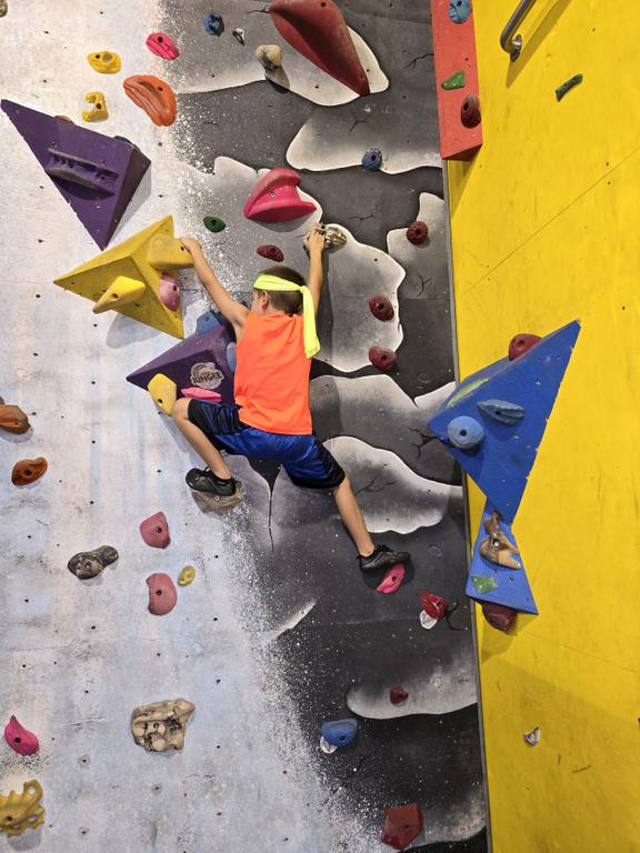 A young boy climbing up a giant rock wall. by The Jungle Movement Academy