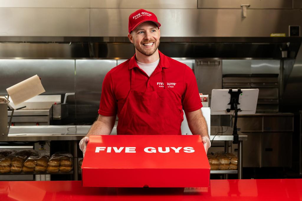A Five Guys employee holds the red Five Guys catering box at the counter. by Five Guys