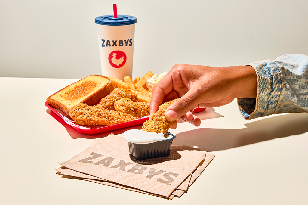 Hand dipping a Zaxbys lemon pepper chicken finger into ranch sauce beside Texas toast, fries, and a drink. by Zaxbys Chicken Fingers & Buffalo Wings